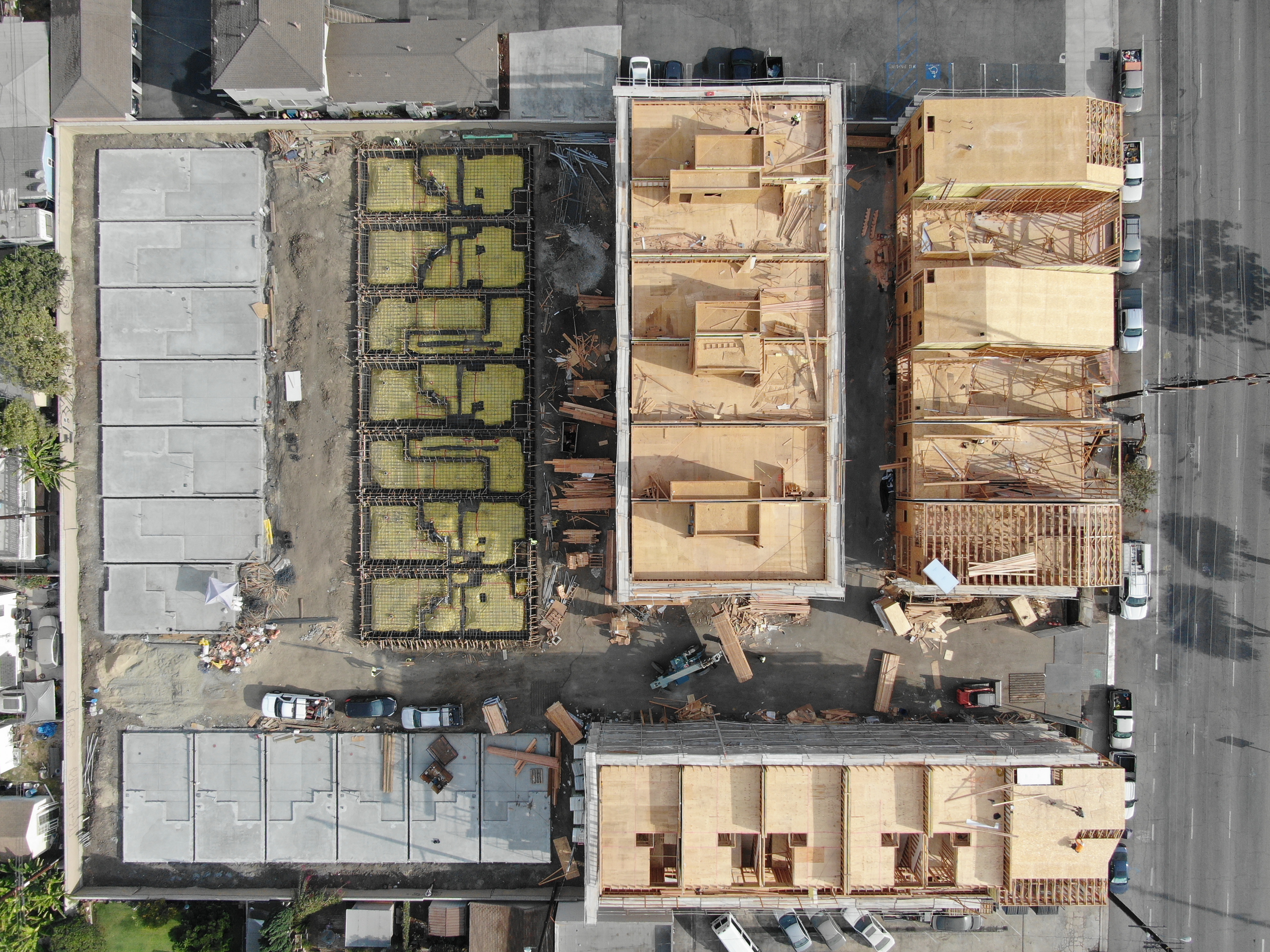 Aerial view of a multi-unit residential development across three construction stages — foundation, framing, and completed structure.