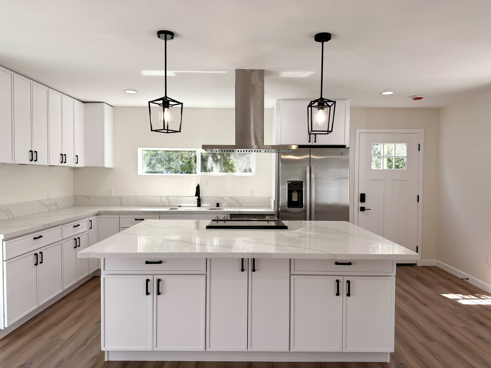 Finished ADU kitchen interior with white shaker cabinets, marble waterfall island, and black lantern pendants.
