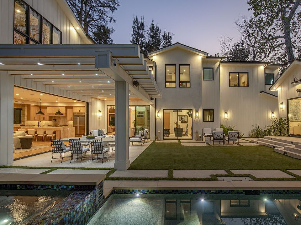 Modern California farmhouse at twilight with pergola, outdoor dining area, and reflecting pool.