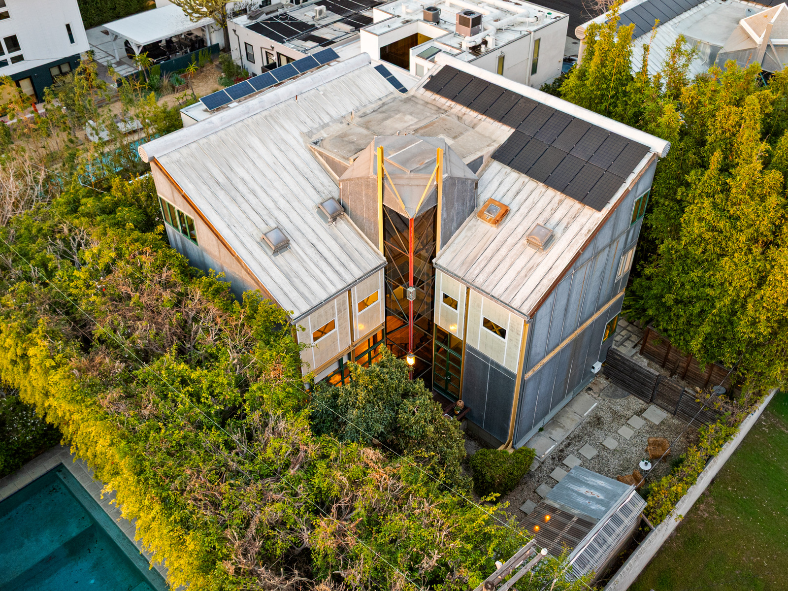 Aerial drone view of a striking modern single-family home with metal-panel roof, solar array, and central glass-walled atrium.